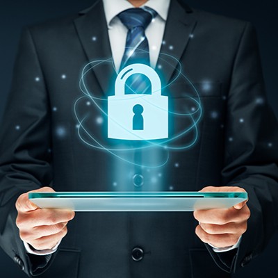 A man stands holding a tablet with a blue hologram of a padlock floating above it with small particles swirling around it.